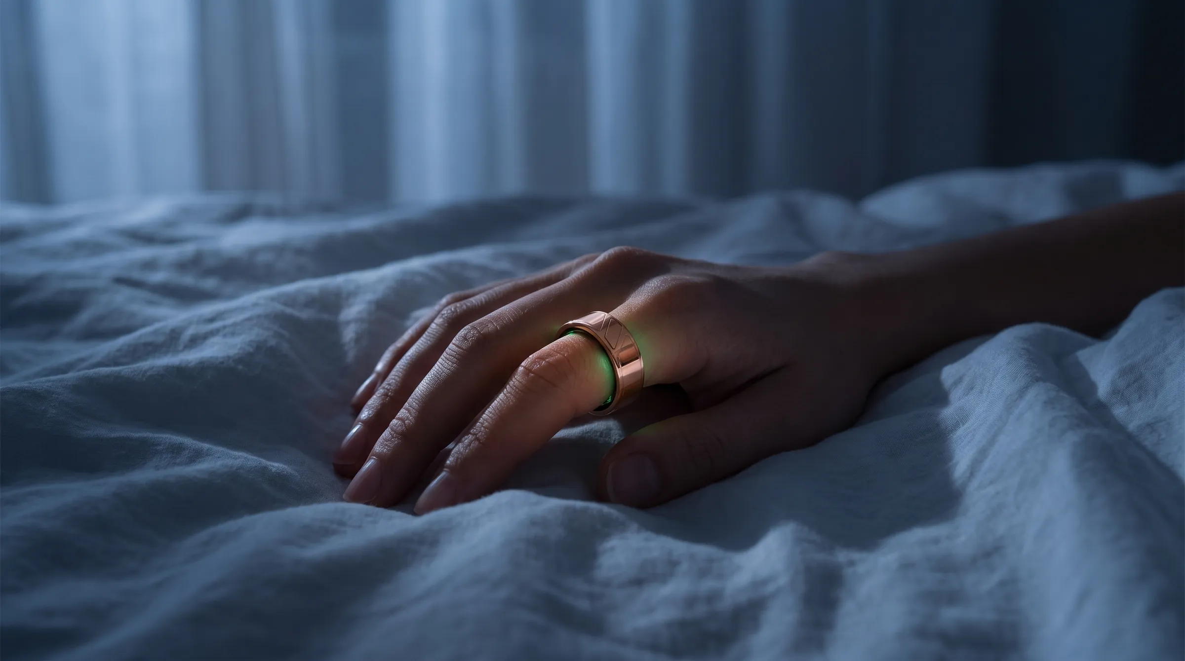 A hand wearing the ring rests on white sheets at night, a faint green light from the sensors