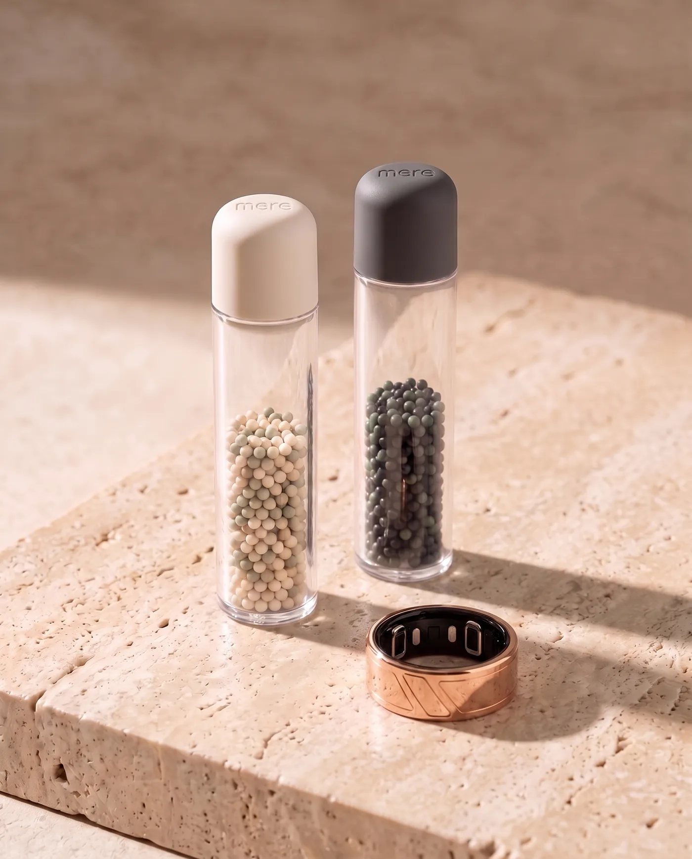 Two clear Mere Formula pods, a Day pod of ivory and sage beads and a Night pod of charcoal and green beads, beside the ring