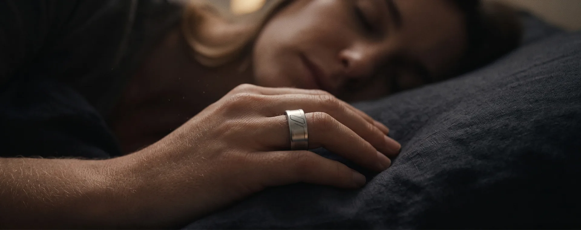 A hand wearing the ring rests on a dark pillow at night